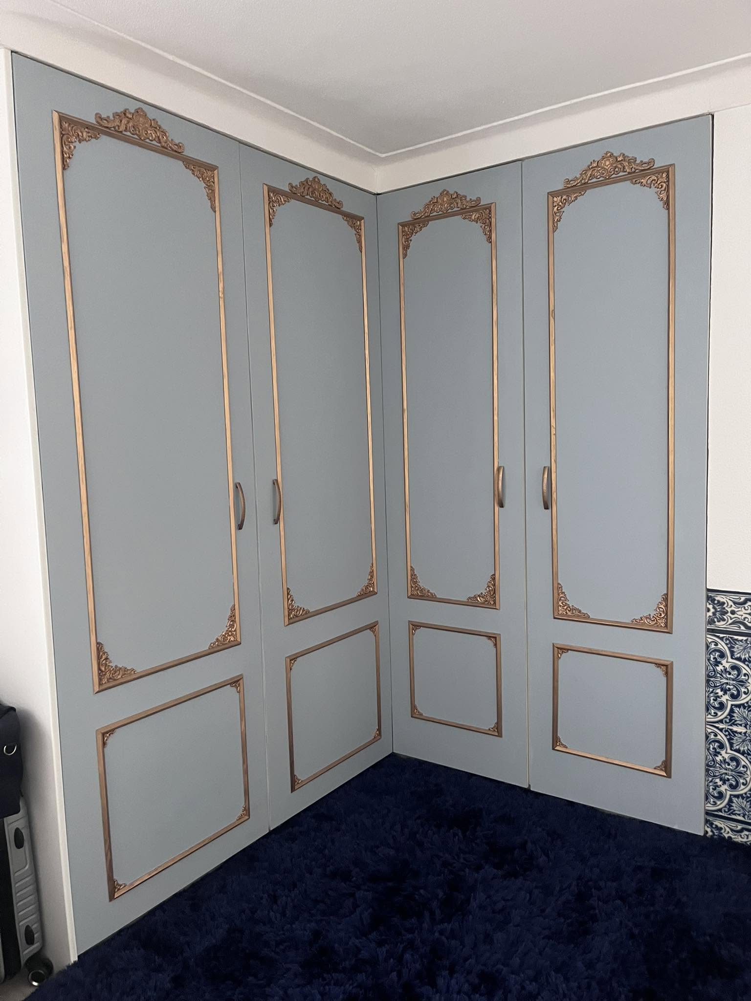 Fitted corner wardrobe doors painted soft blue-grey with gold decorative mouldings and matching handles