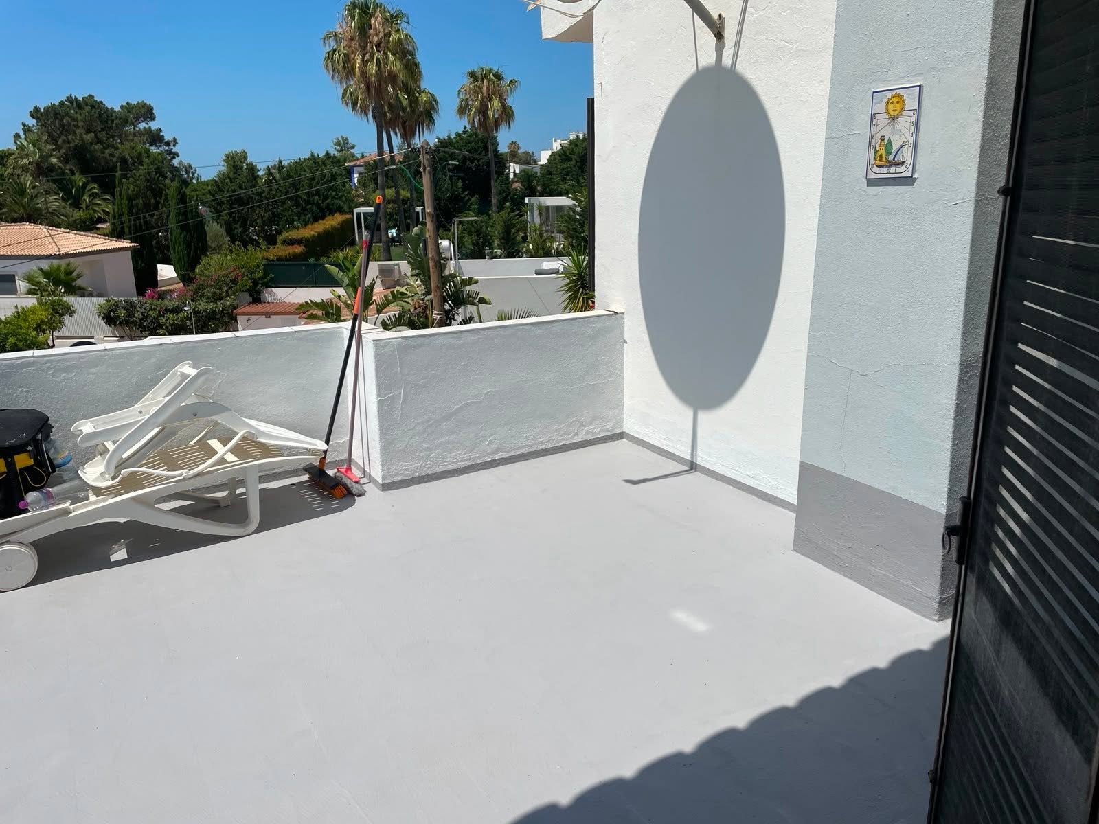 Sunlit Algarve roof terrace with a freshly painted floor and whitewashed walls, palm trees behind